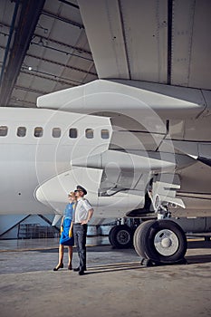 Female air hostess with captain looking to the sky while standing at the airport hangar
