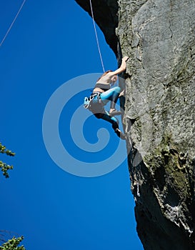 Female alpinist climbing mountain under blue sky.