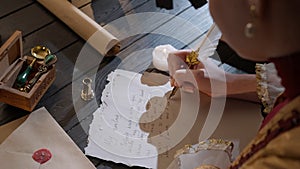 Female in antique outfit writes with feather pen. Over shoulder shot of woman writing a letter with vintage quill