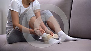 Female applying two-strap ankle wrap, suffering foot edema after sport trauma