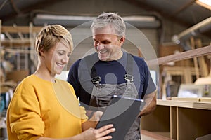 Female Apprentice With Digital Tablet Learning From Mature Male Carpenter In Furniture Workshop