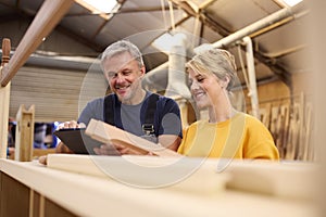 Female Apprentice With Digital Tablet Learning From Mature Male Carpenter In Furniture Workshop