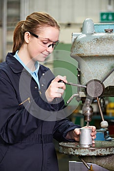 Female Apprentice Engineer Using Drill In Factory