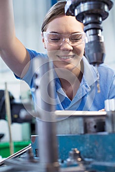 Female Apprentice Using Drill In Factory