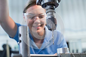 Female Apprentice Using Drill In Factory