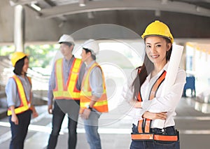 Female architect or engineer holding blue print paper, standing in front of her team smiling and looking at camera