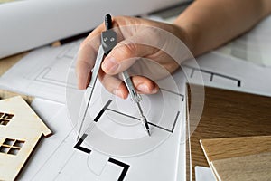 Female architect or interior designer with compass tool, working on home floor plans and structural blueprints at a studio desk.