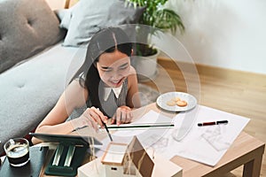 Female architect working on blueprint and using computer tablet at home.