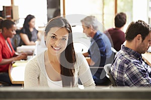 Female Architect Working At Desk With Meeting In Background