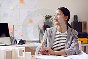 Female Architect Working In Office With Model On Desk Studying Plans For New Building