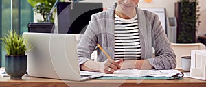 Female Architect Working In Office Sitting At Desk Studying Plans For New Building