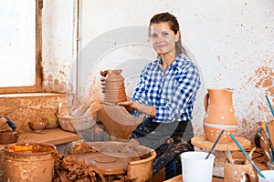 Female artisan in ceramics workshop with pottery wheel and various clay vessels