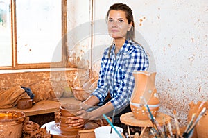 Female artisan with pottery wheel and various clay vessels