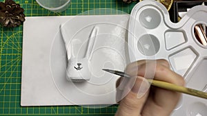 Female artist draws muzzle with brush on clay rabbit.