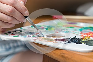 Female artist hand mixing colors with a paintbrush on a color palette