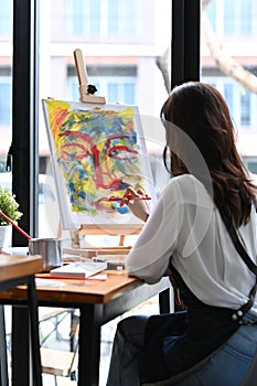 Female Artist painting picture on canvas at art studio.