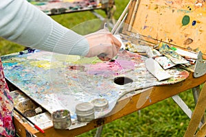 Female artist's hand mixing colors with a paletteknife in a park