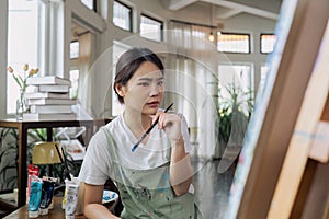 Female artist thinking and hold paintbrush while looking at canvas and pondering about paintin