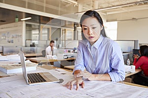 Female Asian architect studying planes in open plan office