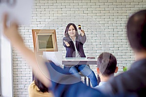 Female asian auctioneer control, holding wooden hammer point to people, and offer bid winner auction highest bidder in final lift,