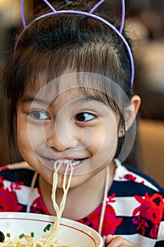 Female asian child while eating noodles. Child eating ramen noodles smiling and enjoying the food. Child eating spaghetti