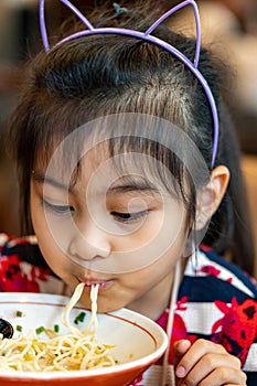 Female asian child while eating noodles. Child eating ramen noodles smiling and enjoying the food. Child eating spaghetti