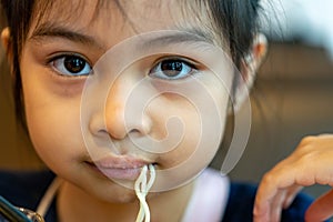 Female asian child while eating noodles. Child eating ramen noodles smiling and enjoying the food. Child eating spaghetti