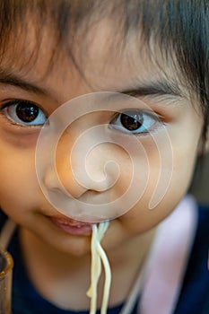 Female asian child while eating noodles. Child eating ramen noodles smiling and enjoying the food. Child eating spaghetti