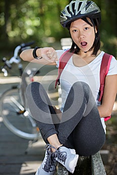 female asian cyclist looking at wristwatch with shock