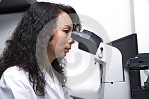 Female Asian scientist looking into eyepieces of microscope