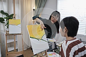 A female Asian teacher teaches kid about acrylic painting in art classroom