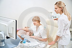Female assistant and doctor sonographer examining thyroid gland of woman patient