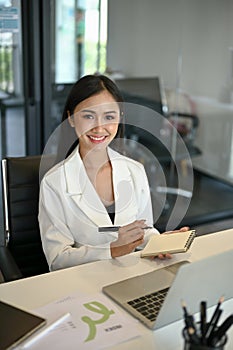 A female assistant or secretary sits at her desk with her notebook and pen in her hands