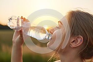 Female athlete being thirsty after running, holding plastic bottle, drinking cold water, resting after jogging workout. Fitness bl