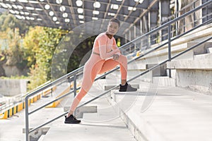 Female athlete doing fitness in a pink sports suit near the sports stadium, African American performs fitness exercises and