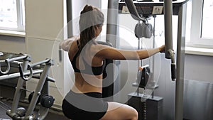 Female athlete doing reverse Pec-Deck flye in gym indoors.