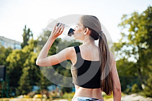 Female athlete drinking from water bottle after workout at stadium