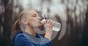 Female athlete drinking water after workout in park