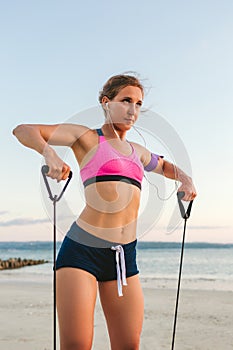 female athlete in earphones with smartphone in armband case doing exercise with stretching band