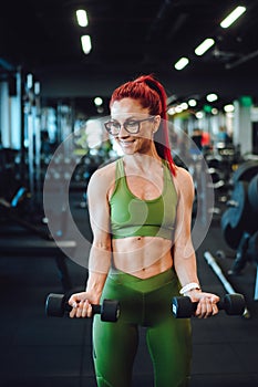 female athlete exercising biceps in the gym, dumbbells details