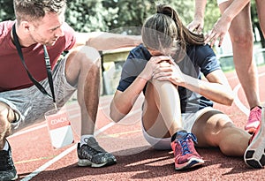 Female athlete getting injured during athletic run training - Male coach taking care on sport pupil after physical accident