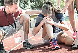 Female athlete getting injured during athletic run training - Male coach taking care on sport pupil after physical accident photo