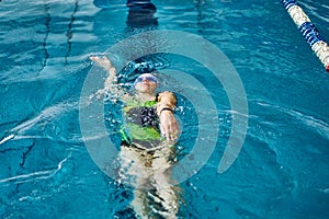 Female athlete in a green-black swimsuit is swimming on his back.