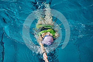 Female athlete in a green-black swimsuit is swimming on his back.