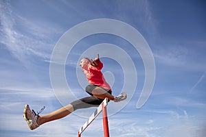 Female athlete jumping above the hurdle during the race