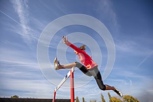 Female athlete jumping above the hurdle during the race