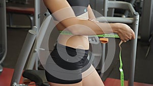 Female athlete measures waist with ribbon in sports club indoors.