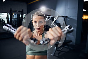 Female athlete is performing dumbbell front raises