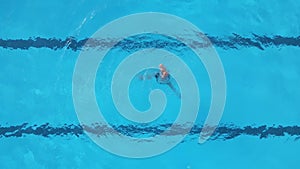 A female athlete performs synchronized swimming routines in an outdoor pool, as seen from the air