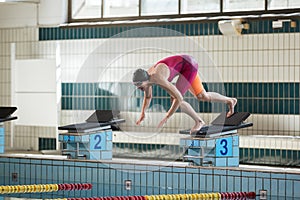 Female athlete preparing for a dive start and jumping into the pool